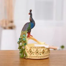 Recipiente ornamental dorado con una figura vertical de pavo real.