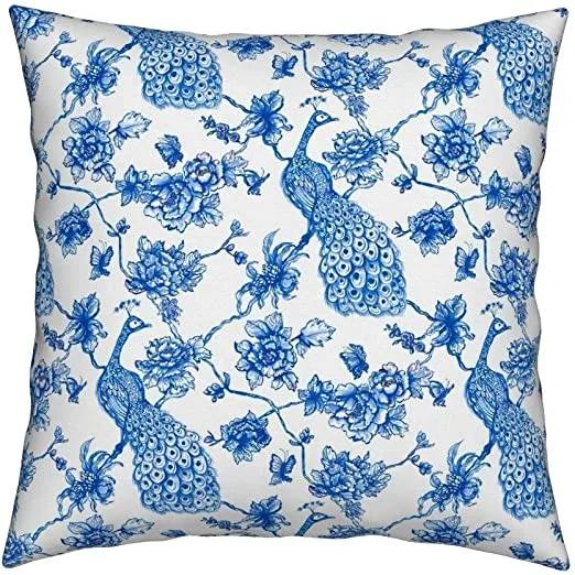 Cojín blanco con pavos reales y ramas de flores dibujados en azul.