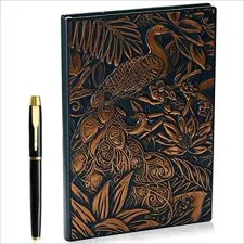 Cuaderno oscuro con un pavo real y ramas de color cobrizo, junto a un bolígrafo.