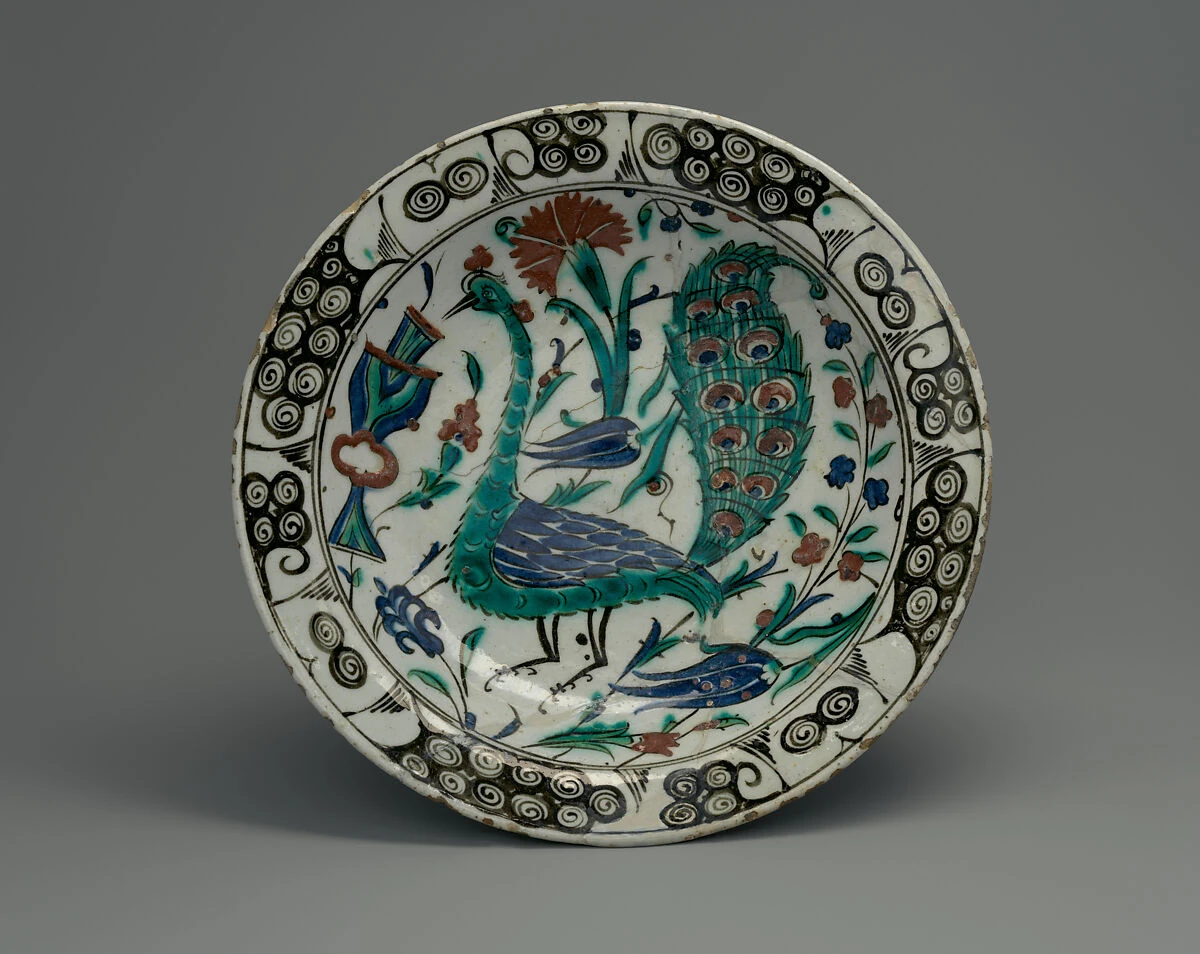 Plato histórico con un pavo real pintado en azul y verde entre flores.