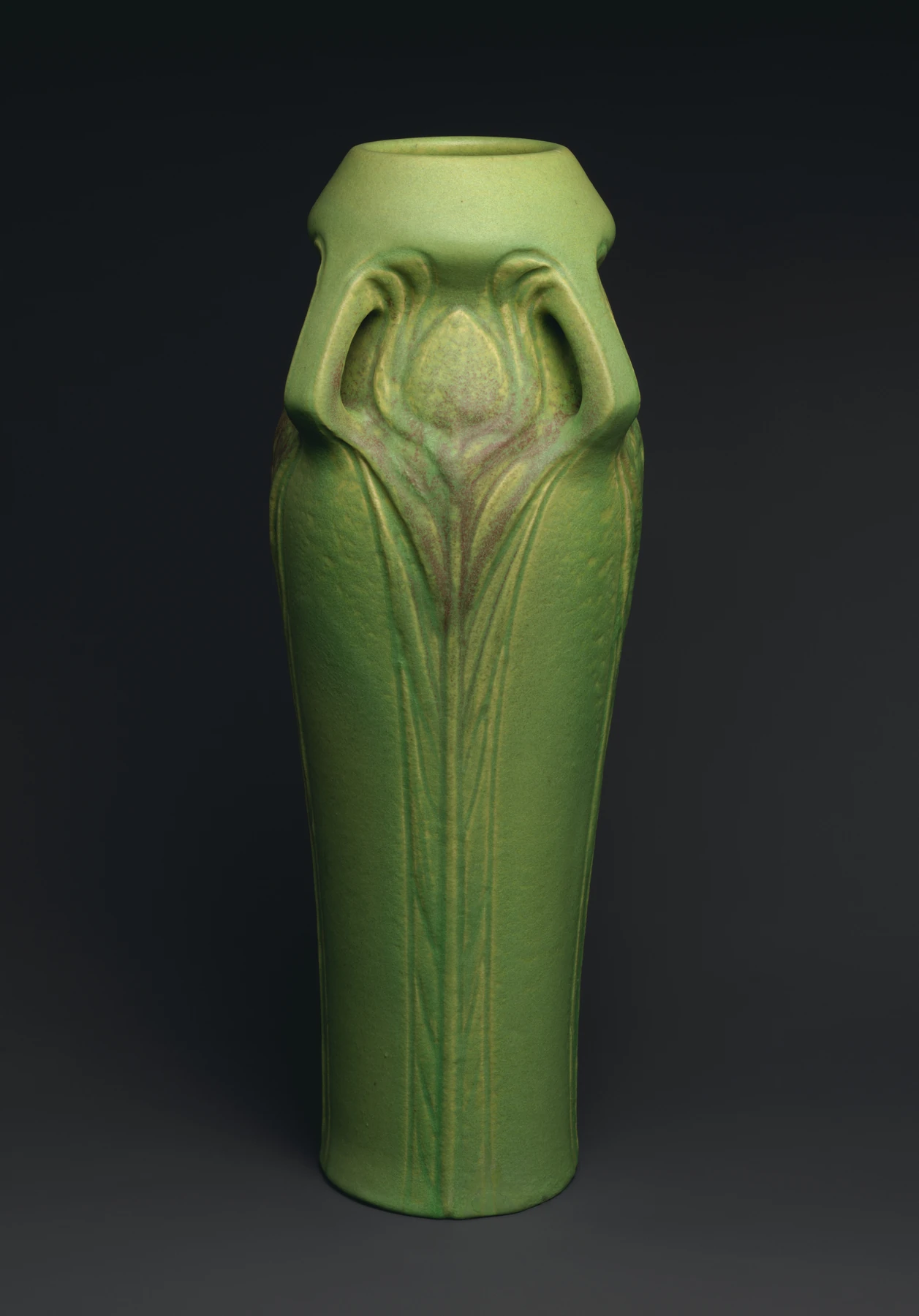 Jarrón verde histórico con plumas de pavo real en relieve sobre un fondo oscuro.