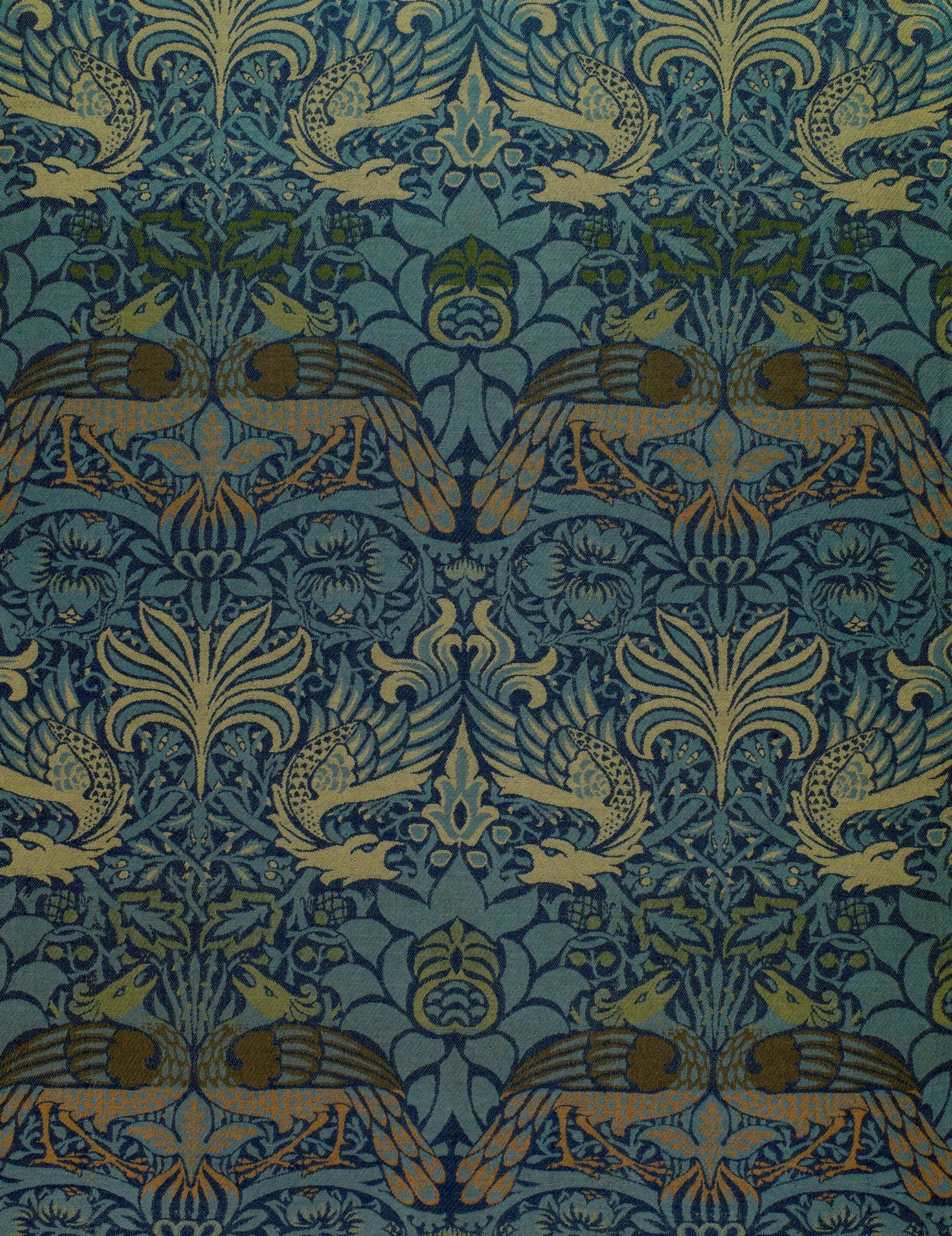 Detalle de un tejido azul y verde con aves y motivos vegetales simétricos.