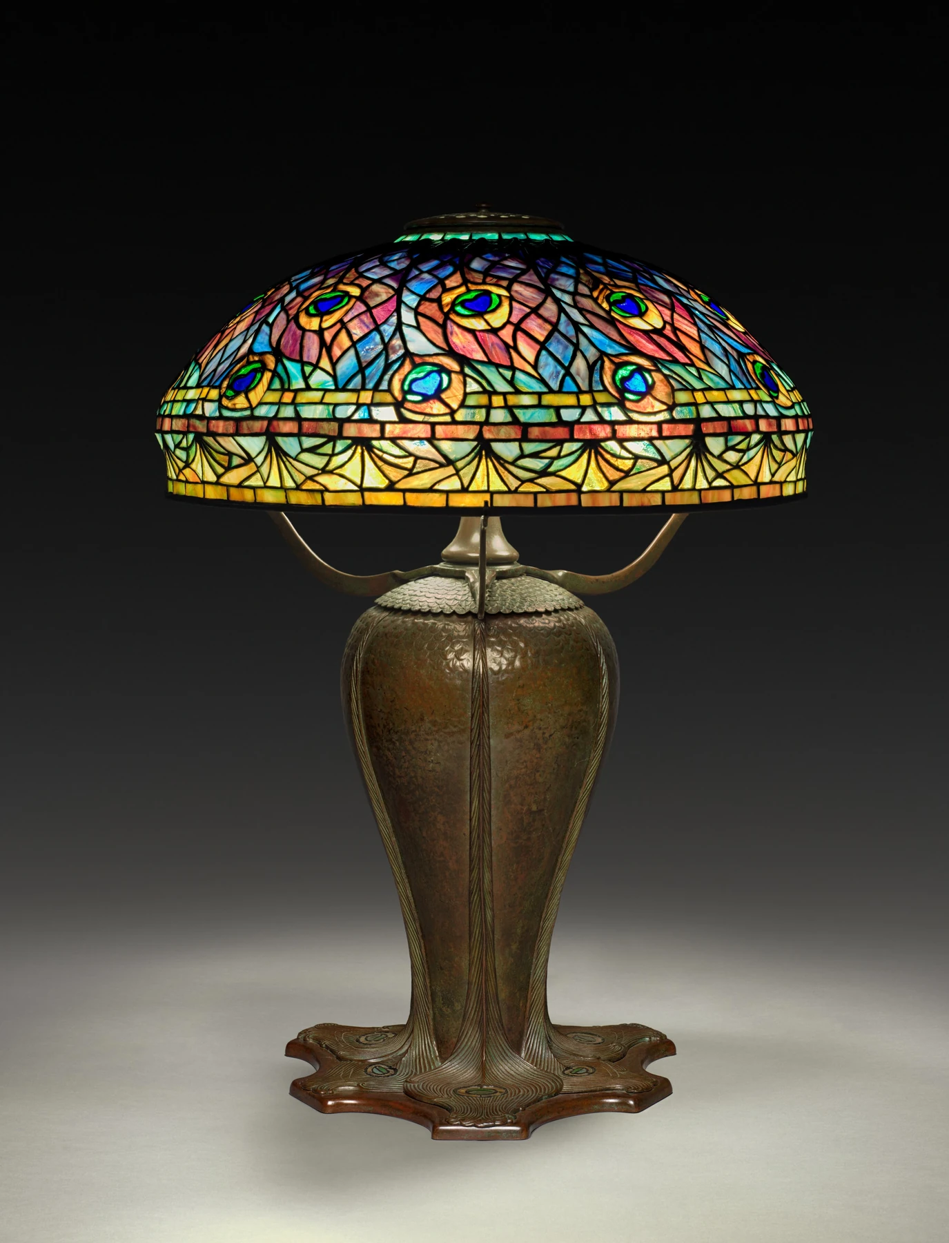 Lámpara histórica Tiffany con pantalla de vidrio de colores y motivos de ocelos de pavo real.