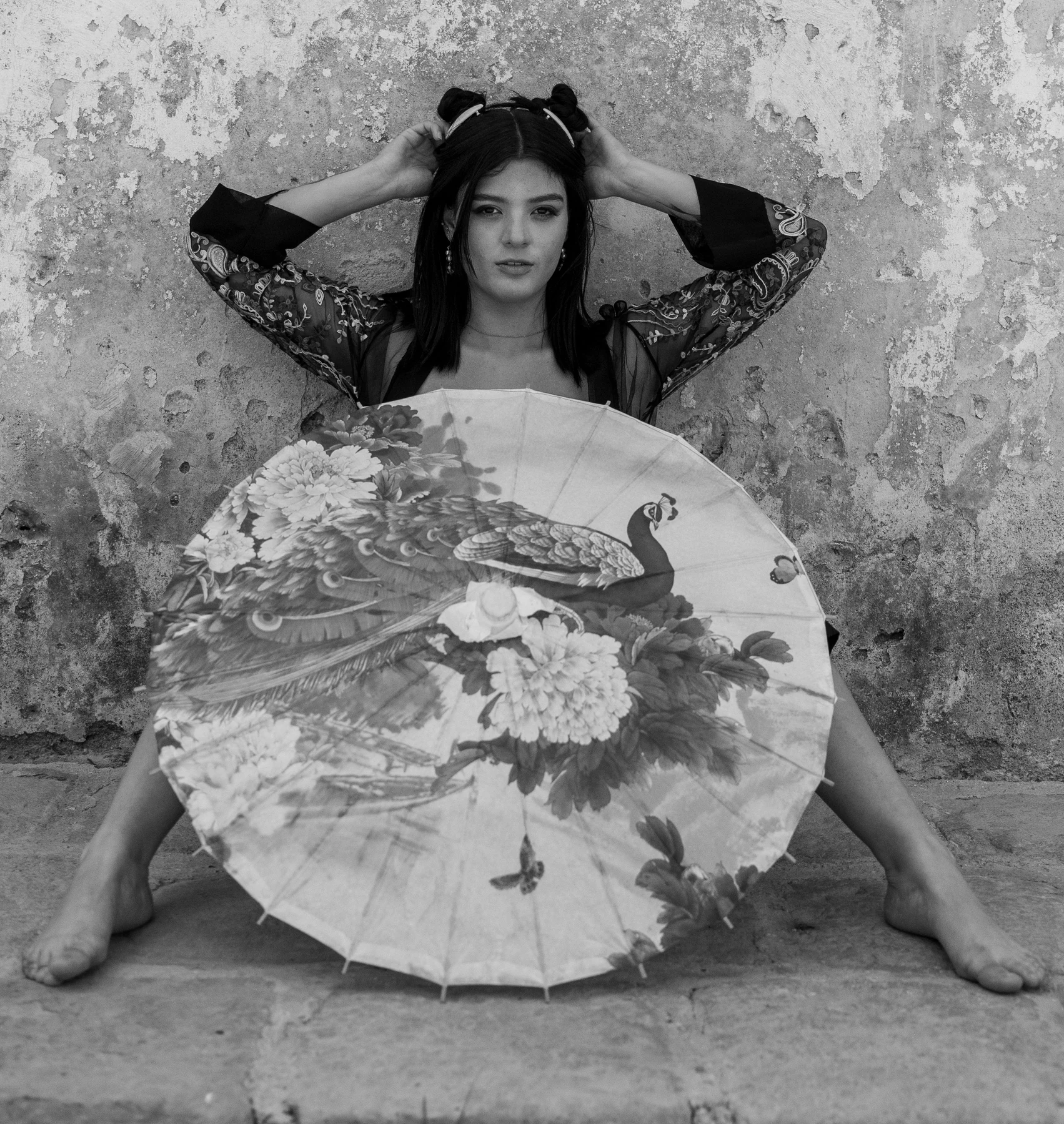 Sombrilla decorativa con un pavo real y flores delante de una persona, en fotografía en blanco y negro.