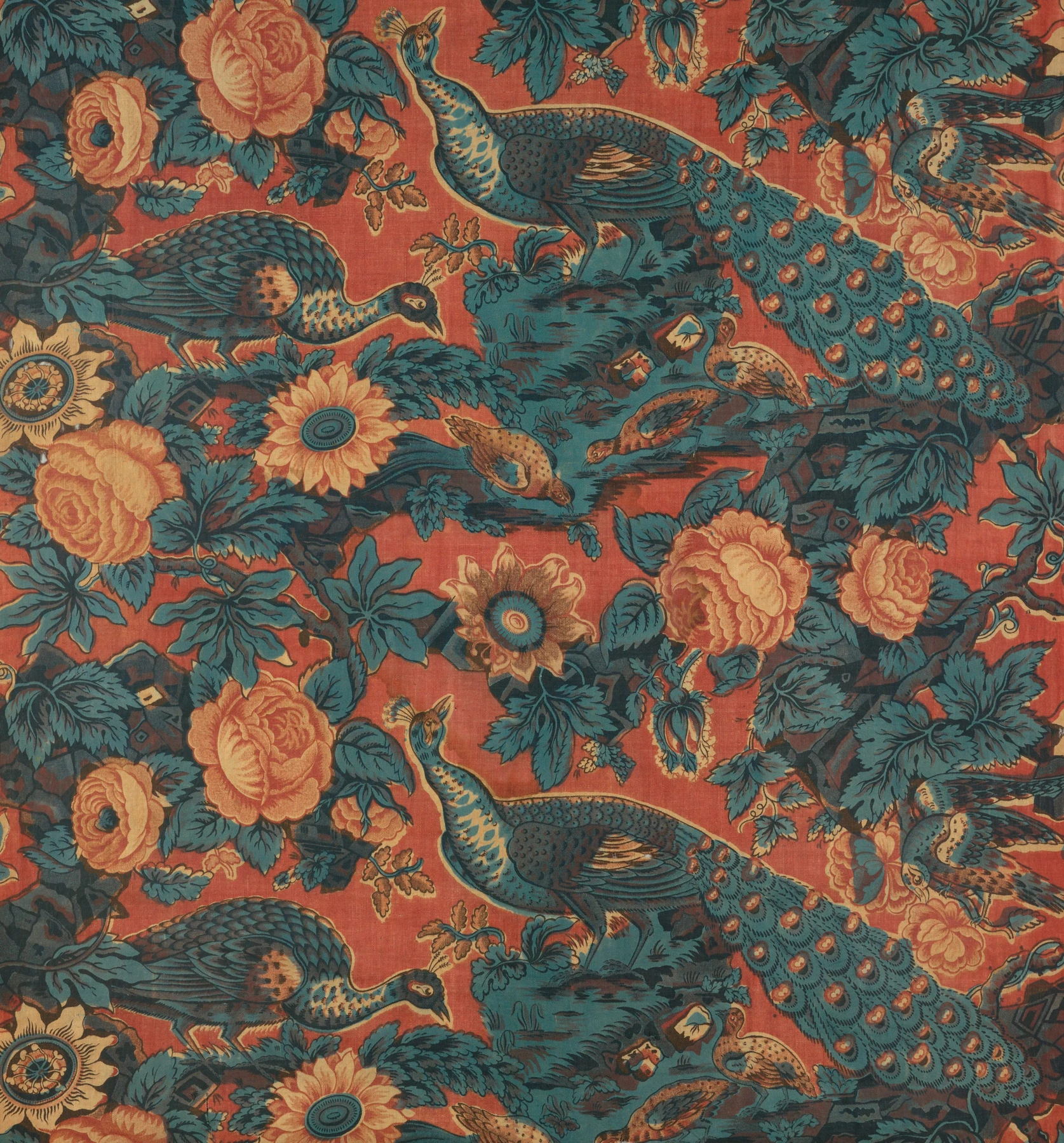 Tejido rojo con pavos reales azules de largas colas, flores y hojas.